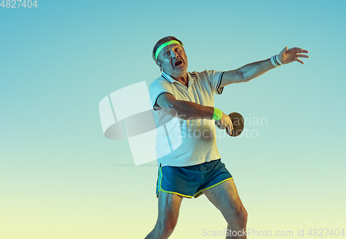 Image of Senior man playing table tennis in sportwear on gradient background and neon light