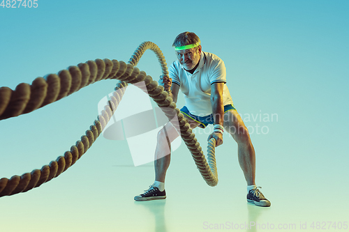 Image of Senior man training with ropes in sportwear on gradient background and neon light