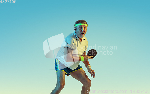 Image of Senior man playing table tennis in sportwear on gradient background and neon light