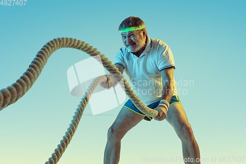 Image of Senior man training with ropes in sportwear on gradient background and neon light