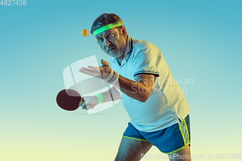 Image of Senior man playing table tennis in sportwear on gradient background and neon light