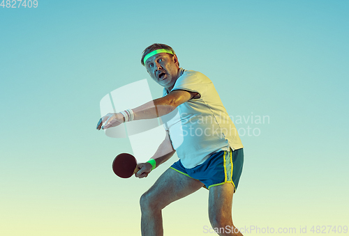 Image of Senior man playing table tennis in sportwear on gradient background and neon light