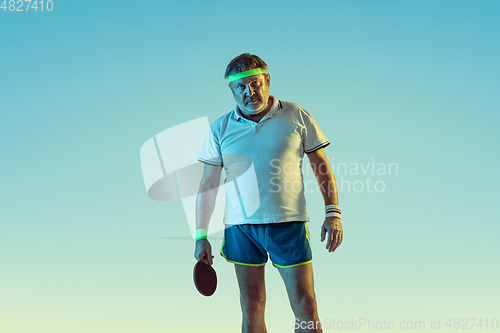 Image of Senior man playing table tennis in sportwear on gradient background and neon light