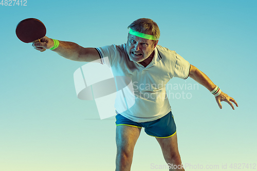 Image of Senior man playing table tennis in sportwear on gradient background and neon light