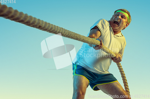 Image of Senior man training with ropes in sportwear on gradient background and neon light