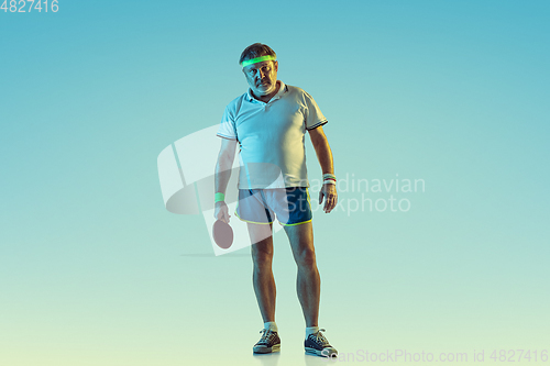 Image of Senior man playing table tennis in sportwear on gradient background and neon light