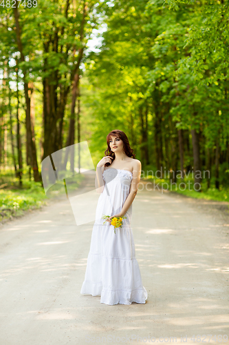 Image of beautiful girl with dandelion flowers on forest road