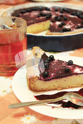 Image of Piece of pie with bilberry on the plate and cup of tea