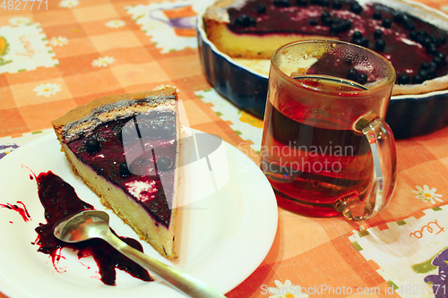 Image of Piece of pie with bilberry on the plate and cup of tea
