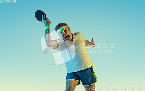 Image of Senior man playing table tennis in sportwear on gradient background and neon light