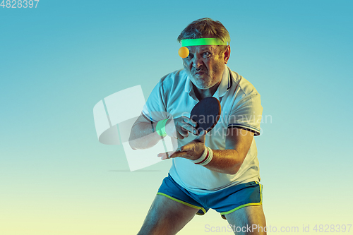 Image of Senior man playing table tennis in sportwear on gradient background and neon light