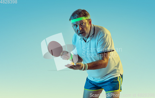 Image of Senior man playing table tennis in sportwear on gradient background and neon light