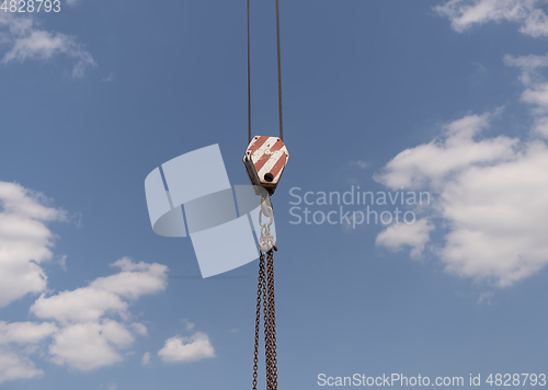 Image of Crane hook with red and white stripes hanging, blue sky in background