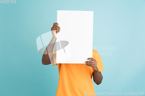 Image of Young African man with blank sheet of paper isolated over blue studio background.