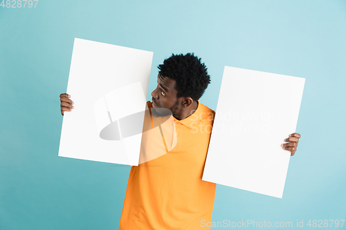 Image of Young African man with blank sheets of paper isolated over blue studio background.