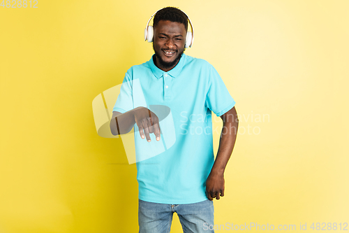 Image of Young African man in headphones isolated over yellow studio background with copyspace.