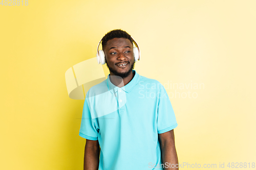 Image of Young African man in headphones isolated over yellow studio background with copyspace.