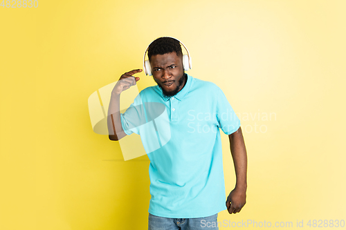 Image of Young African man in headphones isolated over yellow studio background with copyspace.