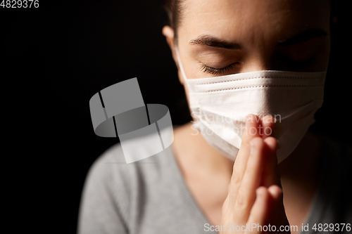 Image of sick young woman in protective face mask praying