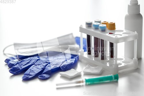 Image of beakers with blood tests, syringe, gloves and mask