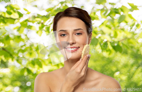 Image of young woman cleaning face with exfoliating sponge