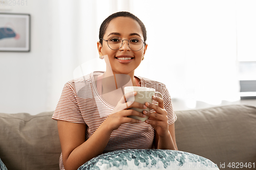 Image of happy african woman drinking tea or coffee at home