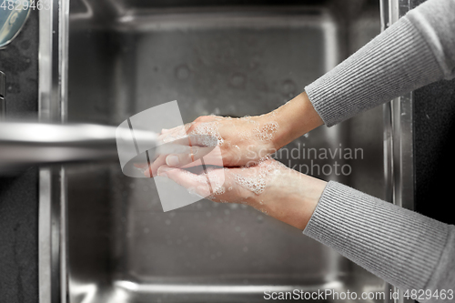 Image of woman washing hands with soap in kitchen