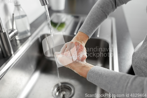 Image of woman washing hands with liquid soap in kitchen