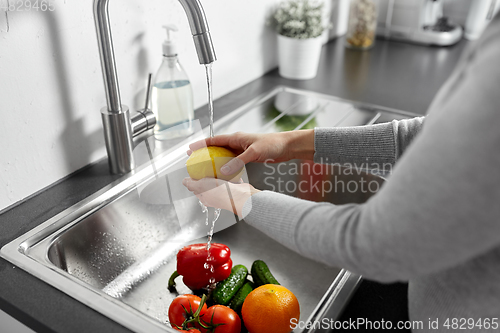 Image of woman washing fruits and vegetables in kitchen