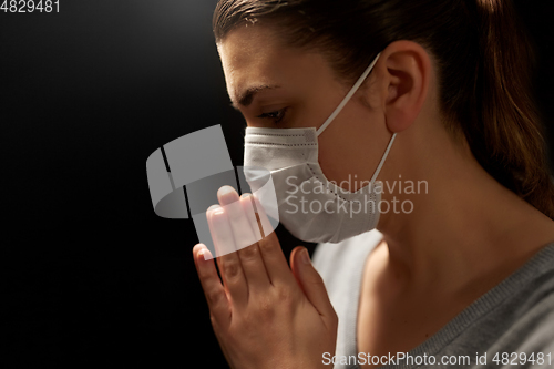 Image of sick young woman in protective face mask praying