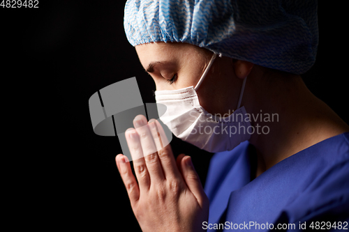 Image of female doctor or nurse in face mask praying