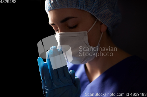 Image of female doctor or nurse in face mask praying