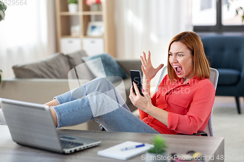 Image of angry woman with smartphone at home office