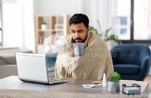 Image of ill indian man in blanket drinking hot tea at home