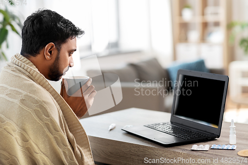 Image of sick young man in blanket drinking hot tea at home