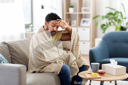 Image of sick young man in blanket having headache or fever