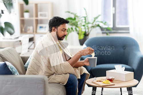 Image of sick young man in blanket drinking hot tea at home