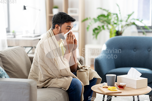 Image of sick man blowing nose in paper tissue at home