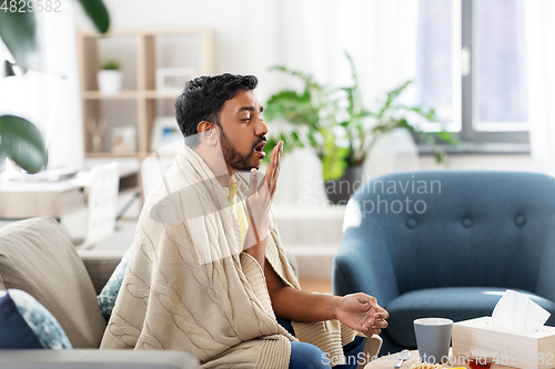 Image of sick young man in blanket coughing at home