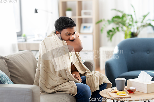 Image of sick young man in blanket coughing at home