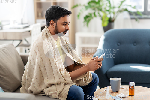 Image of sick young man in blanket with smartphone at home