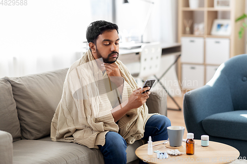 Image of sick young man in blanket with smartphone at home