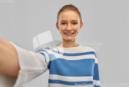 Image of smiling teenage girl in pullover taking selfie