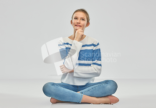 Image of smiling teenage girl sitting on floor and thinking