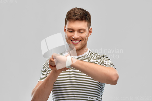 Image of smiling young man looking at smart watch
