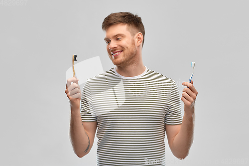 Image of man comparing wooden and plastic toothbrush