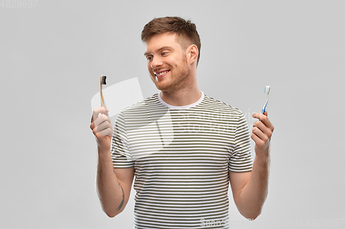 Image of man comparing wooden and plastic toothbrush