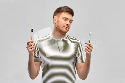 Image of man comparing wooden and plastic toothbrush