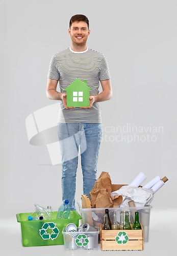 Image of smiling young man with green house sorting waste