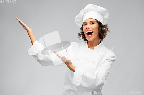 Image of smiling female chef showing something with hands